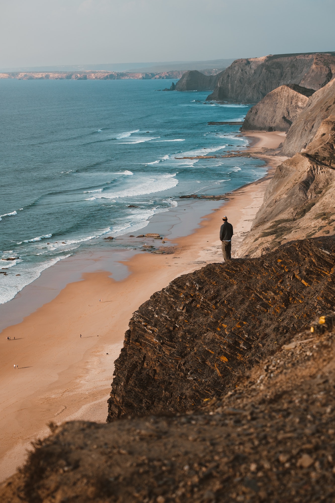 Vertical shot of a person on a cliff looking at the beautiful ocean in Algarve, Portugal