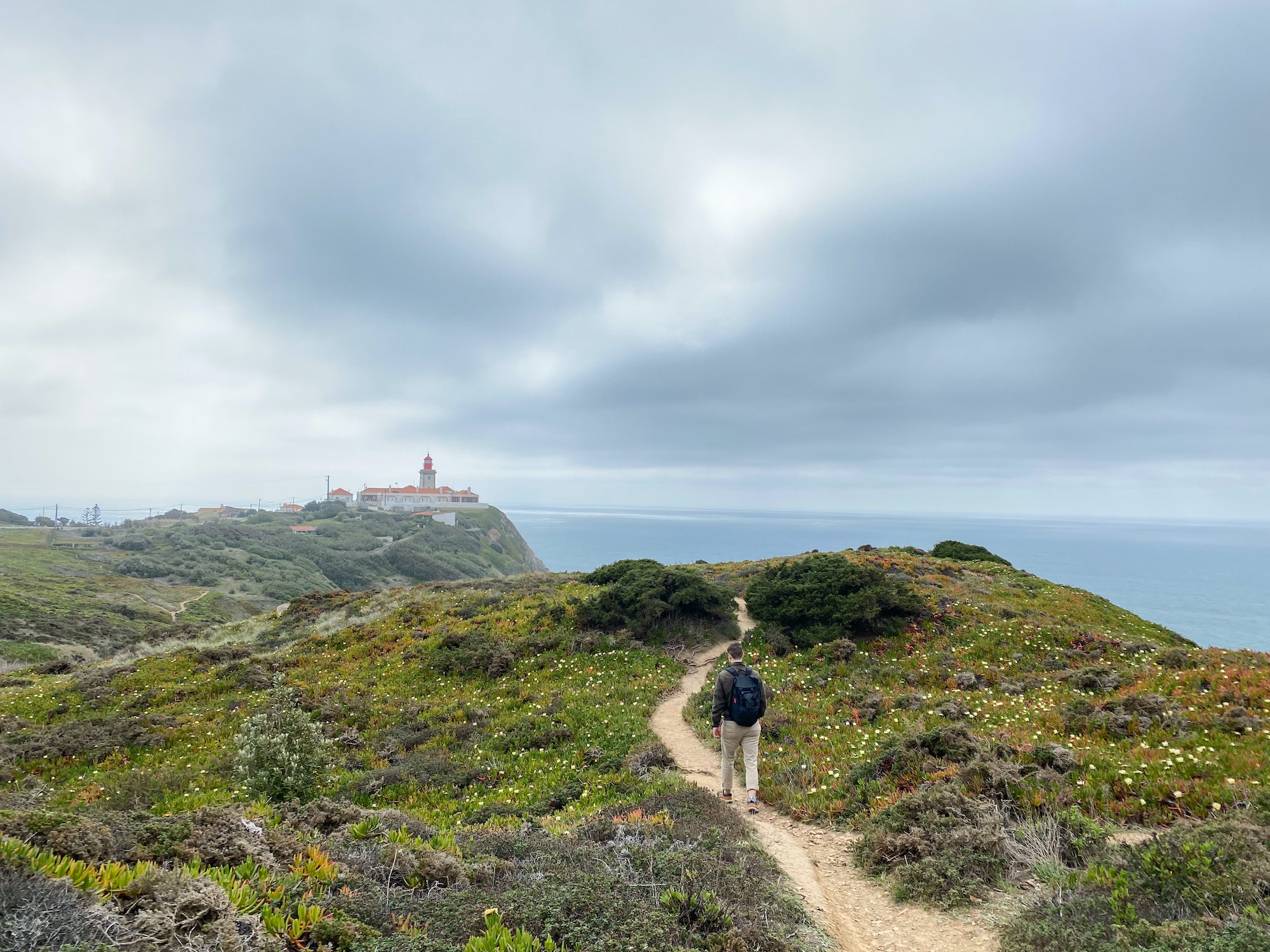 Young man hiking to a lighthouse on the top of the cliff at Cabo da Roca, Atlantic coast, Portugal